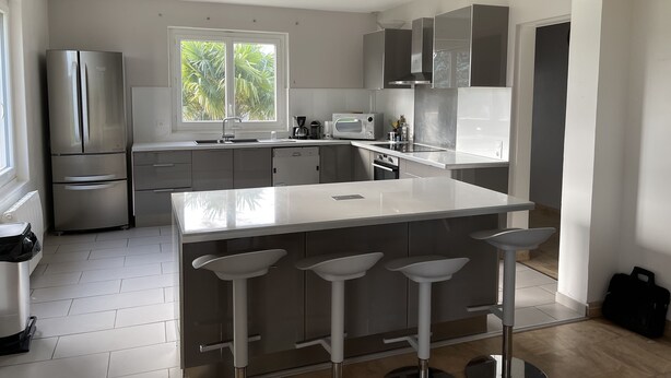 Cocina moderna con una isla grande, taburetes de bar, electrodomésticos de acero inoxidable y una ventana con vistas a zonas verdes.