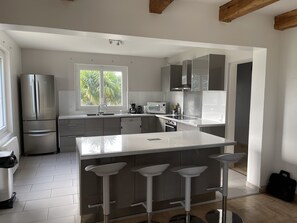 Een moderne keuken met een groot eiland, barstoelen, roestvrijstalen apparatuur en een raam met uitzicht op groen.