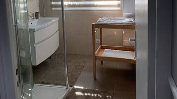 Un baño moderno con cabina de ducha de vidrio, lavamanos blanco y tocador de madera.
