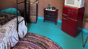 Ett litet rum med en våningssäng, en liten byrå i trä, en mikrovågsugn och ett fönster med gardiner.