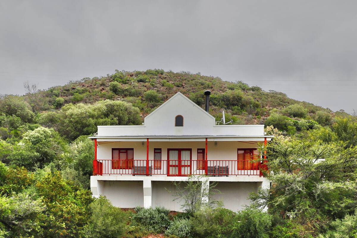 A two-story building with a balcony, surrounded by dense greenery and hills.