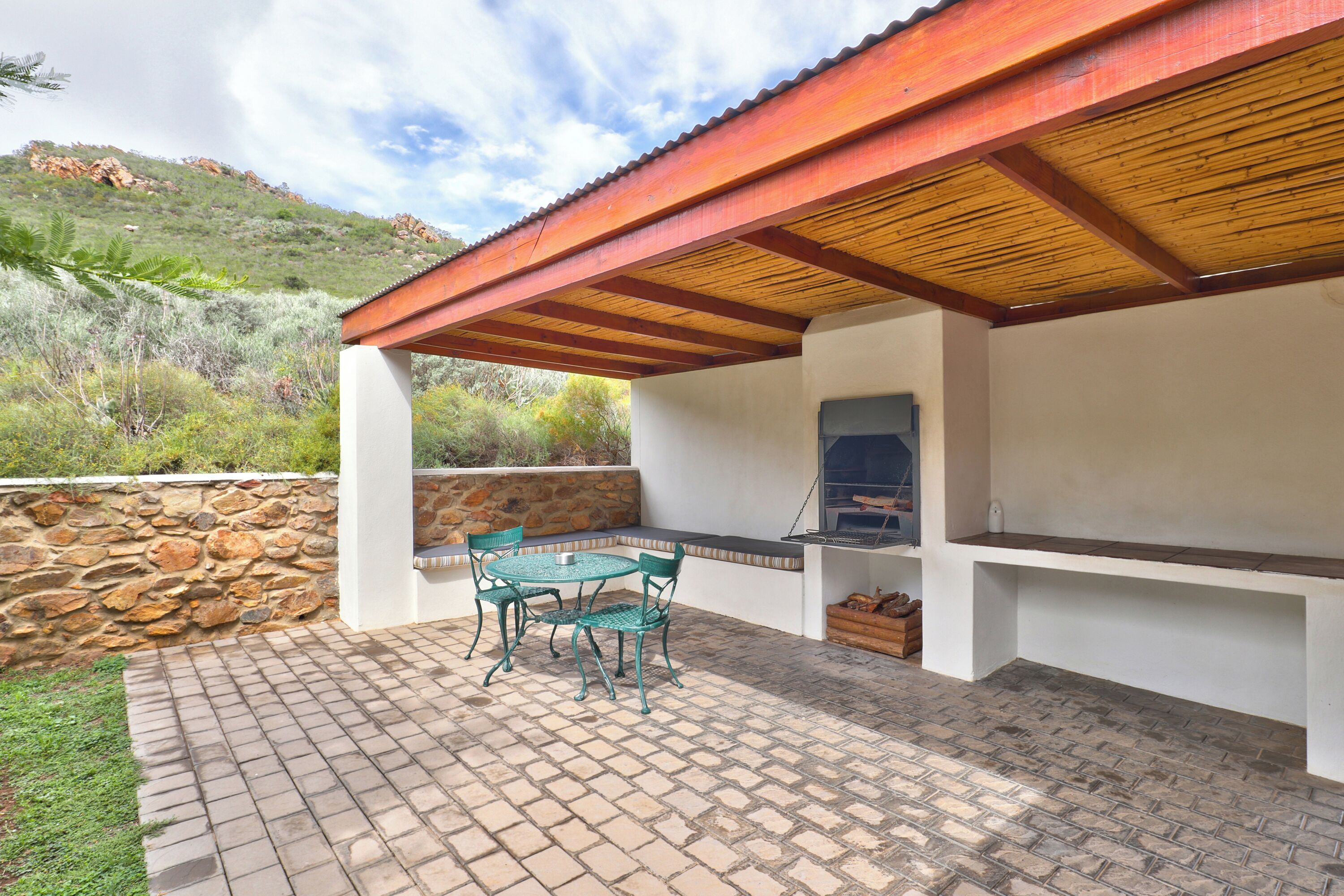 An outdoor patio with a stone wall, a wooden pergola, and a grill area.