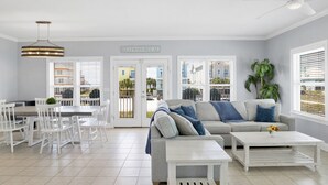 A spacious living area with a grey sofa, white coffee table, and dining table with chairs.