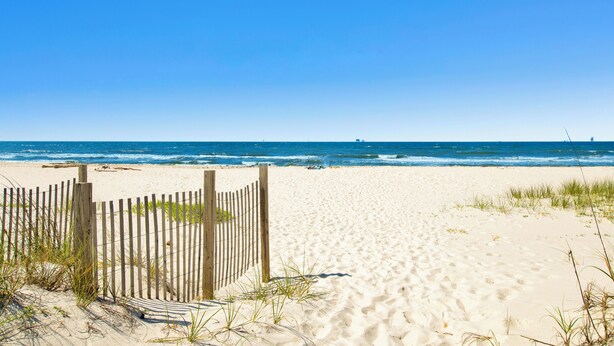 A sandy beach with a wooden fence and waves in the background.