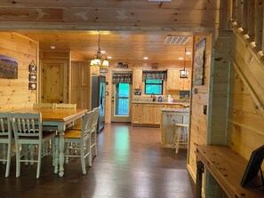 A wooden cabin interior with a dining area, kitchen, and a staircase. - Cozy bear enjoy the peaceful quite and wildlife.    (Gatlinburg)