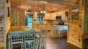 Interior de una cabaña de madera con comedor, cocina y barra.