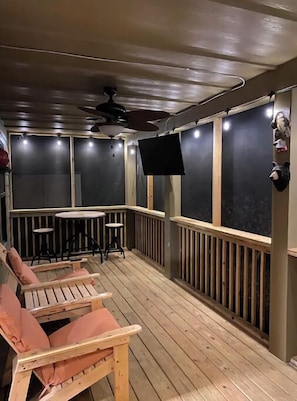Relax in a serene outdoor seating area with a wooden deck, comfortable chairs, and a ceiling fan.