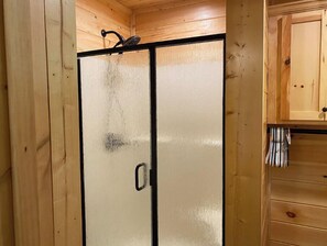 Una habitación con paneles de madera, una puerta corredera de vidrio, un gancho metálico en el techo y un mueble de madera con cajones.