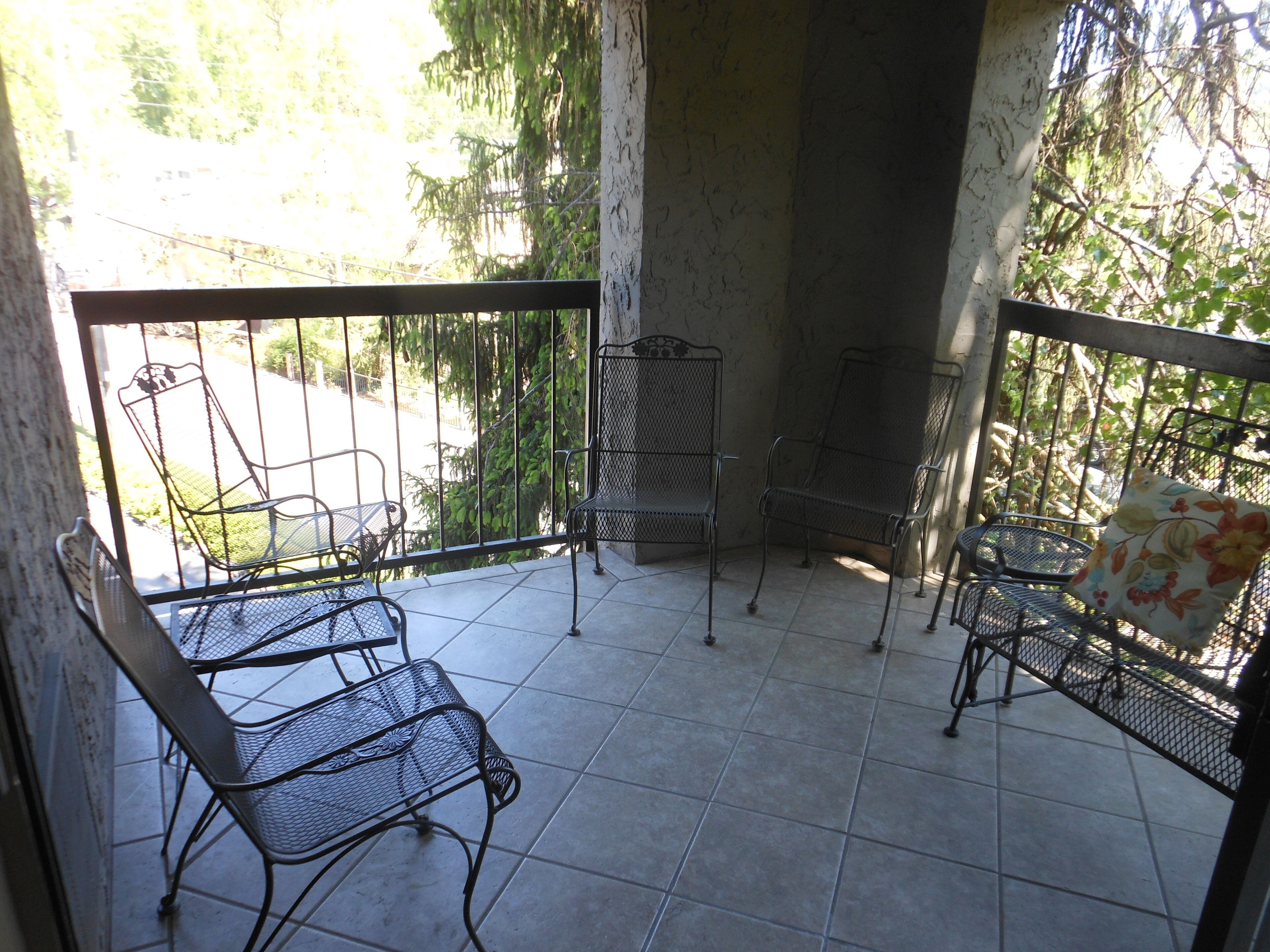 Un balcon avec des chaises et une table en métal, entouré d’une rambarde métallique.