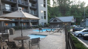 Un espace extérieur avec une piscine, des chaises longues et des parasols, un petit bâtiment doté d’un toit en pente, et une clôture qui délimite l’ensemble.