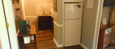 A compact kitchen with a refrigerator, sink, and wooden flooring.