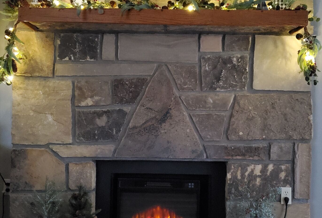 Una chimenea de piedra con diseño moderno, un estante empotrado en la parte superior y fuego a la vista.