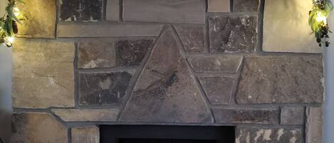 Una chimenea de piedra con diseño moderno, un estante empotrado en la parte superior y fuego a la vista.