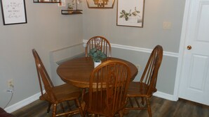 Un coin repas avec une table ronde en bois entourée de quatre chaises en bois, une décoration murale représentant un moulin à vent et des œuvres d’art encadrées.