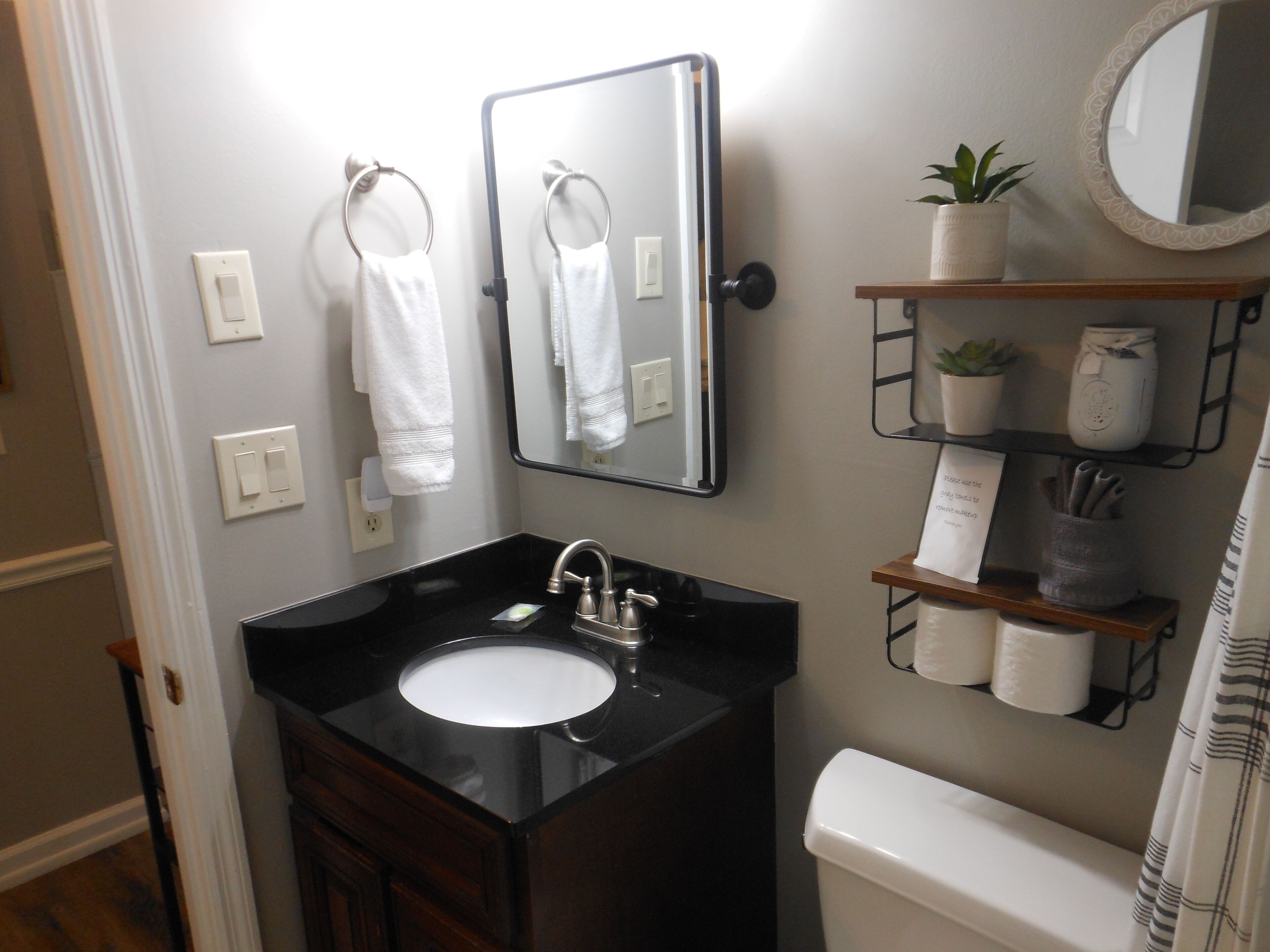 A bathroom with a black sink, a mirror, a toilet, and a shelf with toiletries.