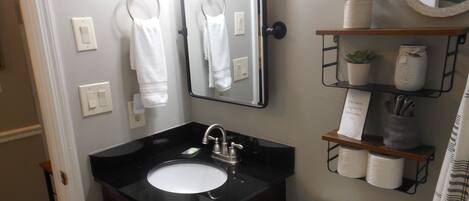 A bathroom with a black sink, a mirror, a toilet, and a shelf with toiletries.