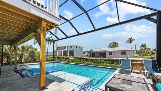 A pool area with a covered seating area, clear skies, and residential buildings in the background. - Heated Pool Home steps to the beach (Fort Myers Beach)