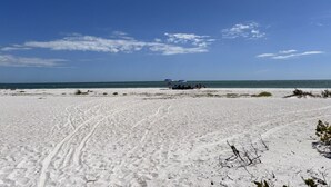 A beach with footprints leading to a group of people under umbrellas. - Heated Pool Home steps to the beach (Fort Myers Beach)
