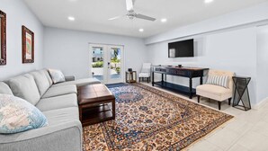A spacious living room with a gray sofa, a coffee table, a patterned rug, a TV mounted on the wall, and a ceiling fan. - Heated Pool Home steps to the beach (Fort Myers Beach)
