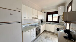 Una cocina con armarios blancos, horno empotrado, cafetera y lavadora.