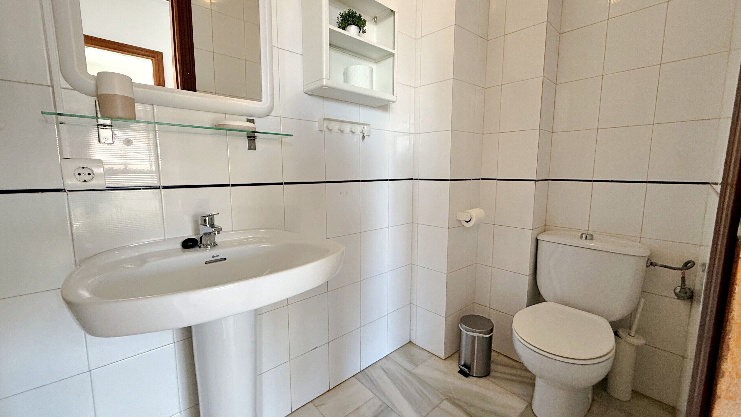 Een badkamer met een wit wastafel, spiegel, toilet en een kleine prullenbak.