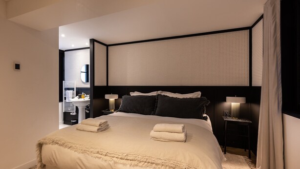 A modern hotel room with a large bed, two bedside tables with lamps, a dark headboard, and a view of the bathroom. - Passocean 1 - Suite in the Heart of Honfleur - Kingsize Bed - Airco (Honfleur)