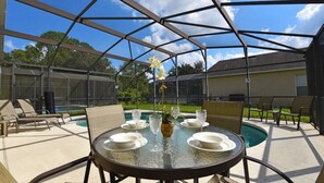 An outdoor patio with a glass table set for dining, surrounded by chairs, and a pool in the background. - Terrific Value 4 Bed Pool Game Spa Home Sandy Ridge (Davenport)
