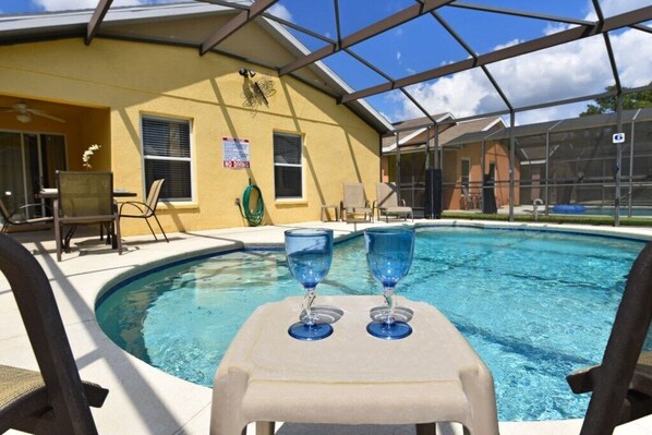 A covered outdoor swimming pool with lounge chairs and a table with two glasses.