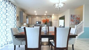 Un comedor con mesa y sillas, una cocina al fondo y una escalera que sube a otro nivel.