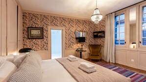 Une chambre d’hôtel avec un grand lit, un lustre, une télévision, une petite table et une chaise.