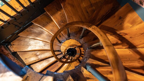 Un escalier en colimaçon en bois, doté d’une rampe centrale et de poutres de soutien en métal.
