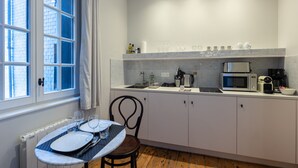 Une cuisine moderne avec des meubles blancs, un plan de travail équipé d’un four à micro-ondes, d’une machine à café et d’une bouilloire. On y trouve également une table à manger avec de l’assiette et des couverts, ainsi qu’une chaise.