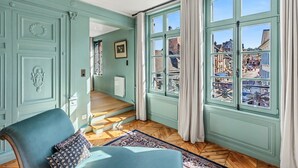 Una habitación con vistas a un pueblo a través de amplios ventanales, un sofá azul y una escalera de madera.
