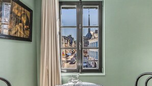 Una mesa de comedor con un vaso de agua y una copa de vino, un cuadro en la pared, y una ventana con vistas a edificios.