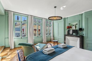 Habitación de hotel con cama, una silla, escritorio, mesita pequeña, espejo y chimenea.