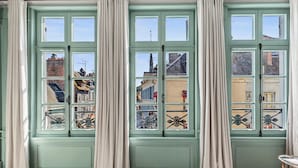 Una habitación con ventanas amplias, piso de parquete y vistas a edificios.