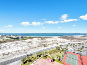 A coastal view with a road, a tennis court, and a distant body of water. - Sun Sation I 4/4 I Beach Chairs Available (Navarre Beach)