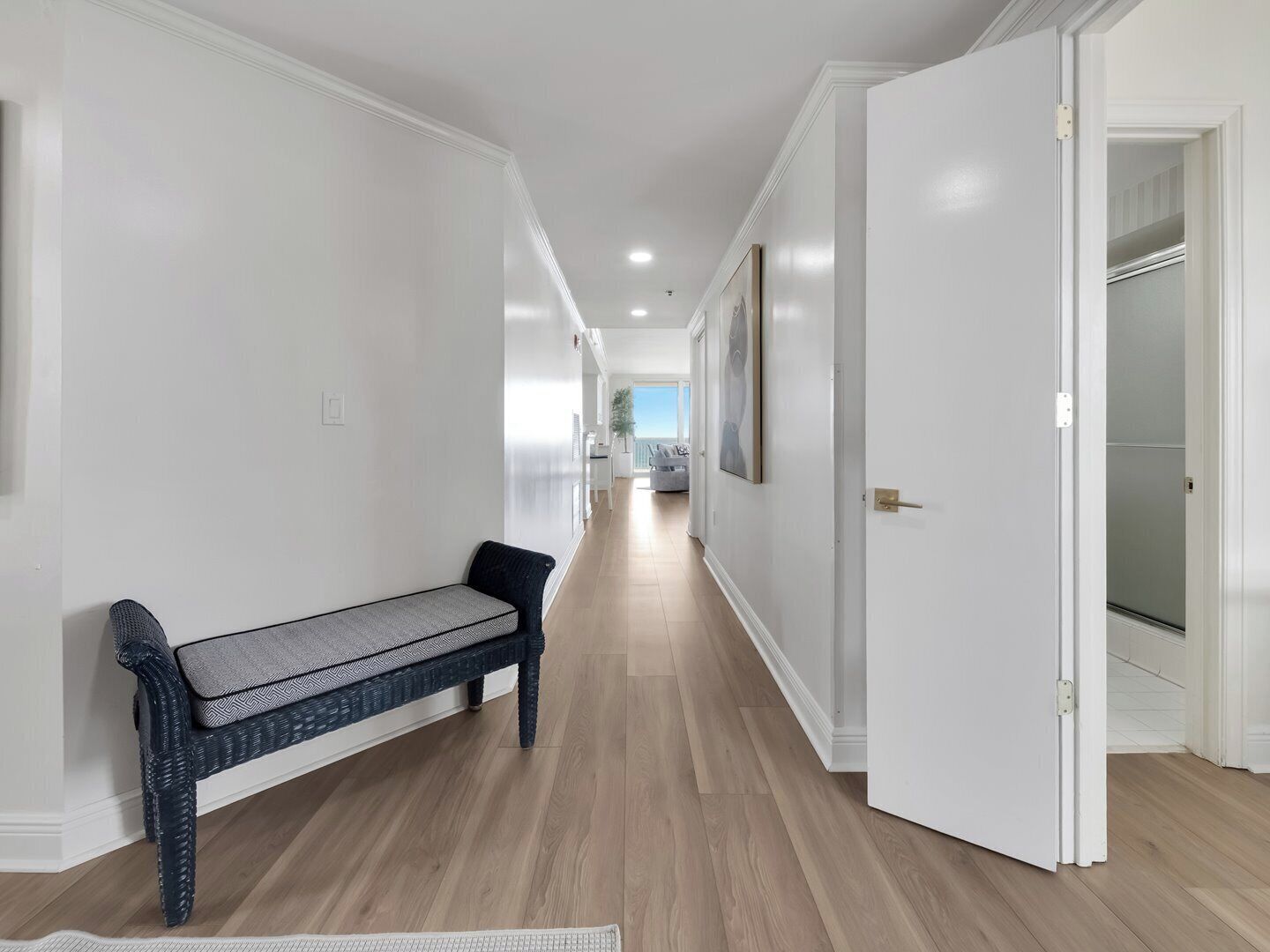 Un couloir avec un banc, une porte donnant sur un placard et une vue sur une pièce avec un balcon.