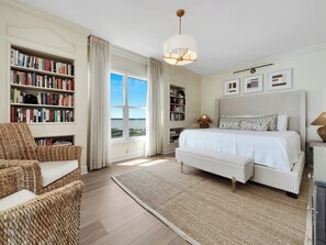 A bedroom with a large bed, a bookshelf, a chair, and a view of the outdoors. - Sun Sation I 4/4 I Beach Chairs Available (Navarre Beach)