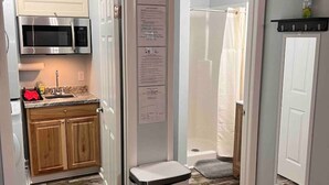 A compact kitchen with a microwave, wooden cabinets, and a trash bin.