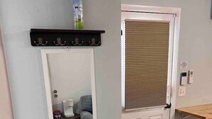 A room with a white door, a mirror, a small table with a chair, and a wooden floor.