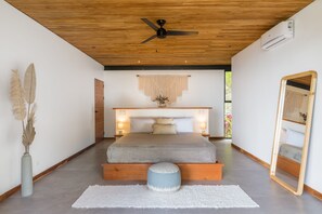Un dormitorio moderno con techo de madera, una cama con cabecera de madera, un otomano redondo y un espejo grande.