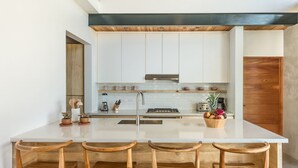 Une cuisine moderne avec des meubles blancs, un îlot central doté de tabourets de bar et un plafond en bois.