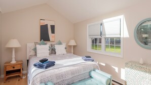 A bedroom with a bed, two bedside tables, a window with blinds, and a wall-mounted artwork.