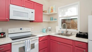 A kitchen with pink cabinets, a white microwave, a stove, and a sink.
