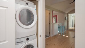 A laundry area with two stacked washing machines, a wooden floor, and a red-framed door leading to another room.