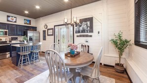 A modern kitchen with dark cabinets, a stainless steel refrigerator, and a dining area with a wooden table and white chairs. - Romantic Smoky Mtn Cabin w/Hot Tub, Views, Arcade (Sevierville)