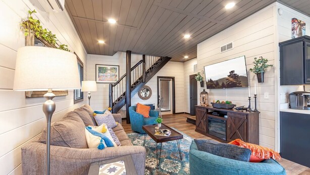 A spacious living room with a staircase, a fireplace, and a large window. - Romantic Smoky Mtn Cabin w/Hot Tub, Views, Arcade (Sevierville)