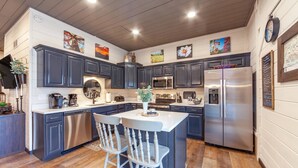 A modern kitchen with dark cabinets, stainless steel appliances, and a central island with two white chairs. - Romantic Smoky Mtn Cabin w/Hot Tub, Views, Arcade (Sevierville)