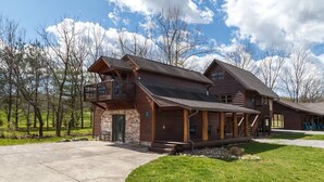 A two-story log cabin with a balcony, a stone foundation, and a covered porch. - Romantic Smoky Mtn Cabin w/Hot Tub, Views, Arcade (Sevierville)